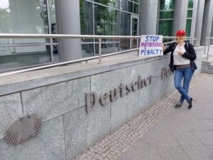 Judith Münter vor dem Deutschen Bundestag mit dem Plakat "Stop Motherhood Penalty"